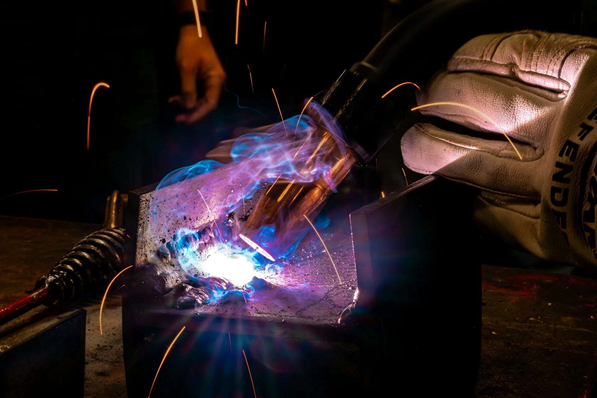 Gloved hand welding steel, throwing off bright sparks