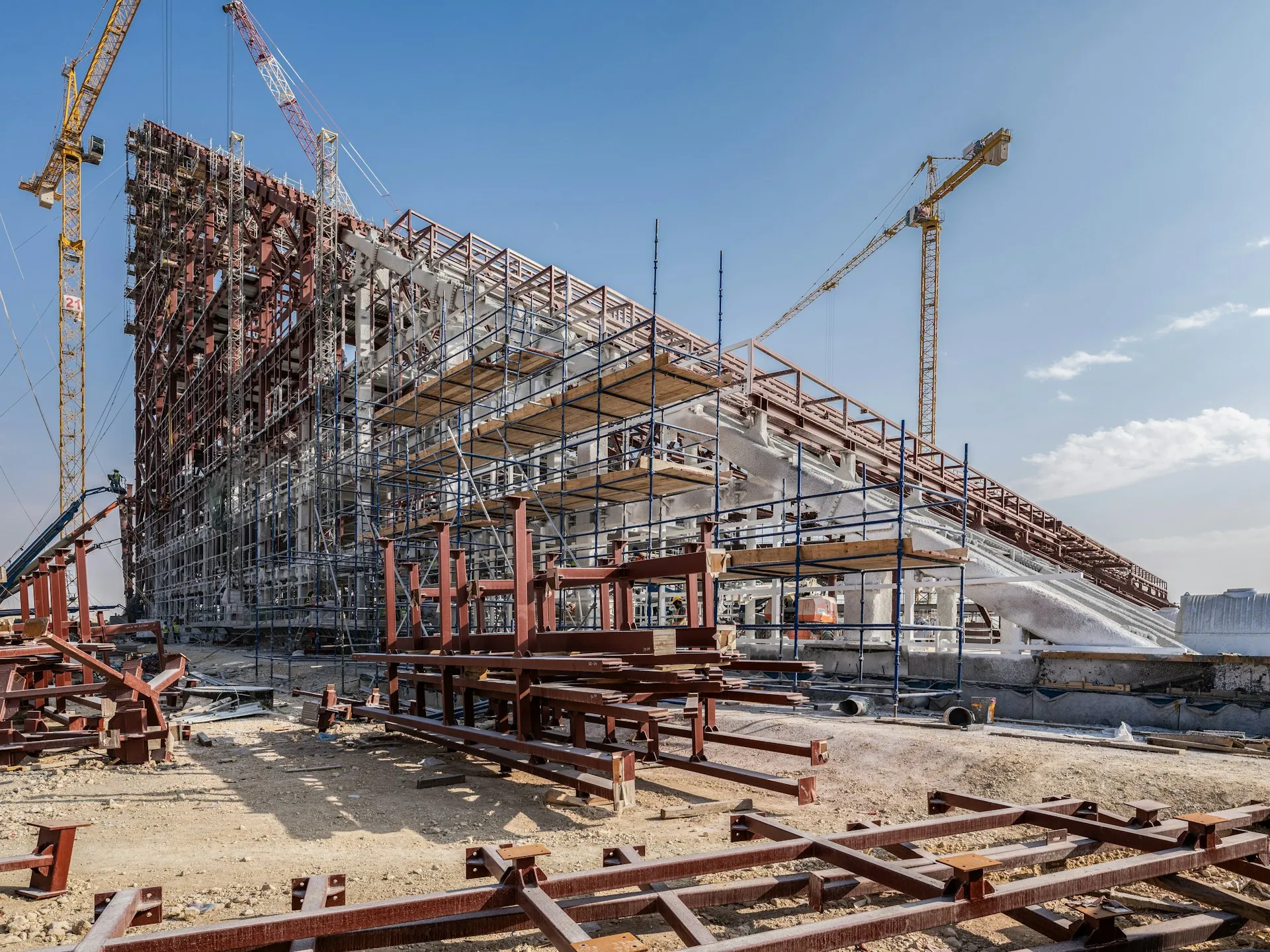 Large steel-framed building under construction with tower cranes